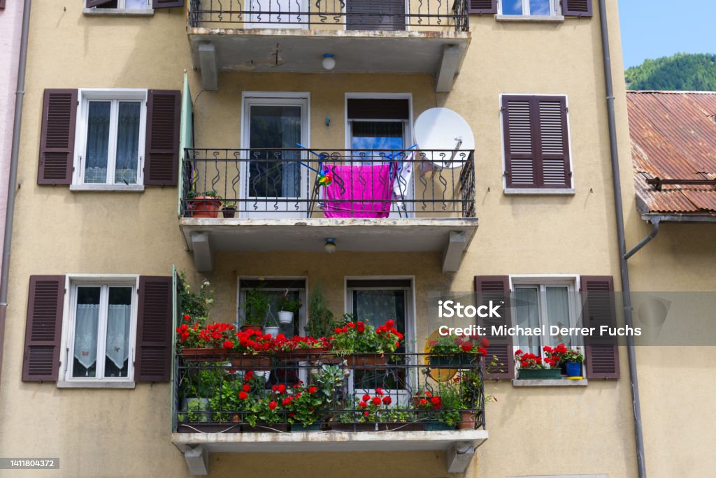 Balconies of apartment house with laundry rack, satellite dish and red flowers on a sunny summer day. Photo taken June 25th, 2022, Airolo, Switzerland. Building Exterior Stock Photo