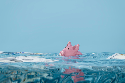 Debt or inflation concept of piggy bank sinking underwater with 100 dollar bills in the water.