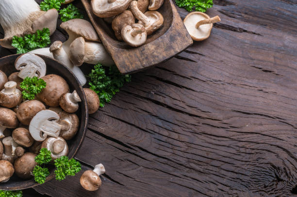 istock Different brown colored edible mushrooms on wooden table with herbs. Top view. 1411811336