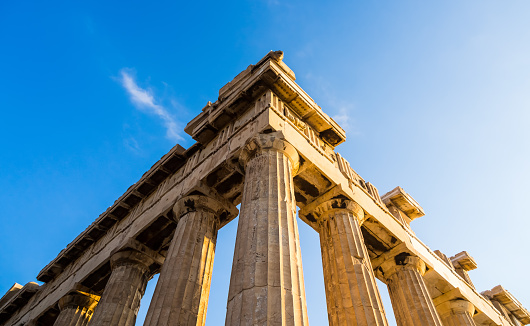 Close-up view of a corner of ancient Greek temple, remaining Doric columns and entablement at clear blue sky in low sun sunlight. Classical architecture, archaeology, history and design.