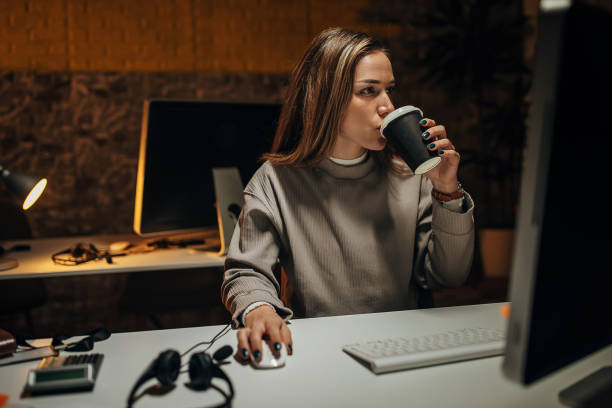 One woman, beautiful young woman working on computer in office late at night, she is drinking coffee to stay awake.