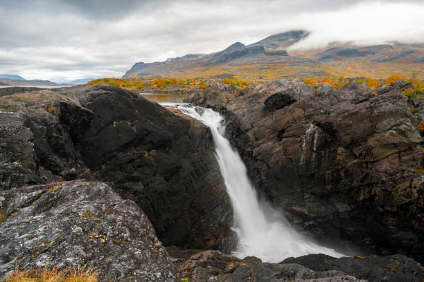 istock Mighty scenic waterfall under dramatic sky. Stuor Muorkke waterfall in Stora Sjofallet national park, Sweden. Adventure in arctic wilderness. Autumn colors in the arctic. 1411816937