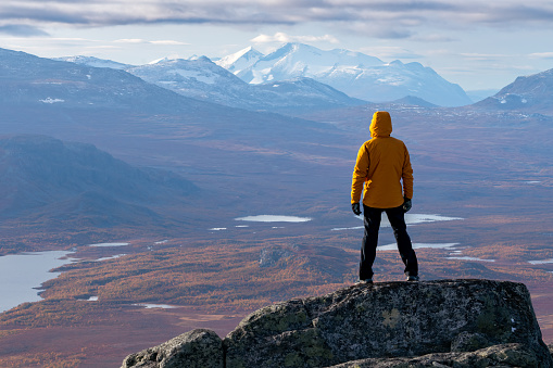 Male hiker overlooking epic view of vast arctic landscape of Stora Sjofallet National Park, Sweden, on autumn day. Mountains and valleys of Lapland. Ahkka massif. View from the top of Lulep Gierkav