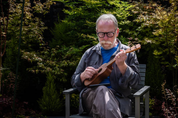 Retired man sitting in his garden in Scotland practising his new hobby playing a ukulele