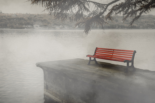 A red park bench at the lake in the fog, concept of grief and loss