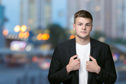 Young businessman stands on a blurred background of the evening city.
