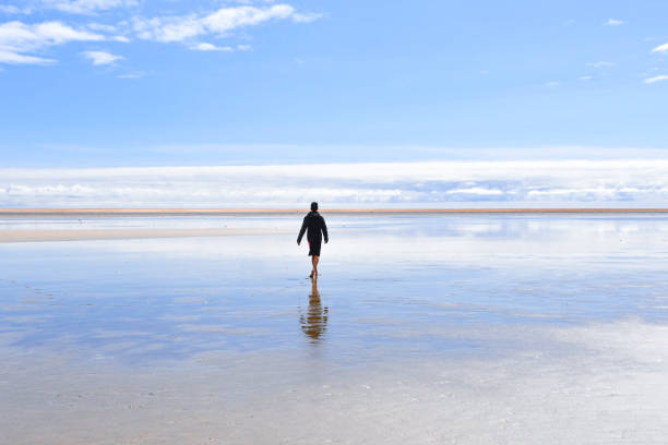 Boy dressed in black with reflection on the water walking to the beach with orange sand - Fjord in the north of Iceland Europe