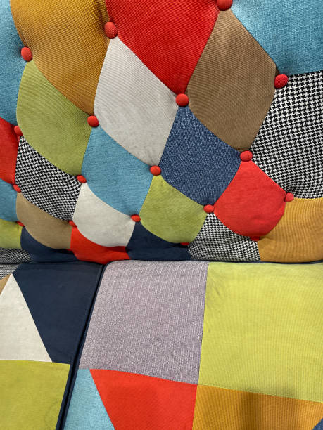istock Full frame image of harlequin patterned tight back sofa with red material covered buttons and patchwork cushioned seats, multicoloured material geometric pattern, focus on foreground 1411825449