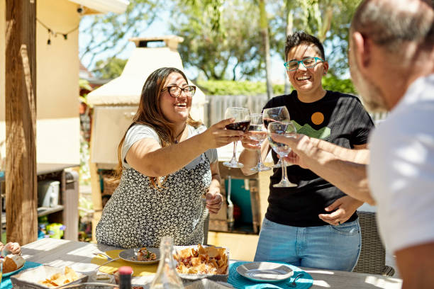 Smiling friends enjoying celebratory toast with wine Lesbian and gay couples in casual weekend attire standing at outdoor dining table and touching glasses before sitting and beginning their meal. florida food stock pictures, royalty-free photos & images