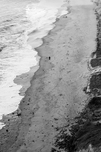 Black and white aerial shot of single person walking along the coastline. Person walking on a sandy beach of Helgoland island, Germany. Concept for wandering, solitude, meditation, meaning of life