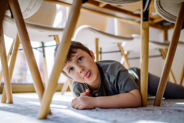 istock Little boy hiding under the chair at home and making grimace. 1411831563