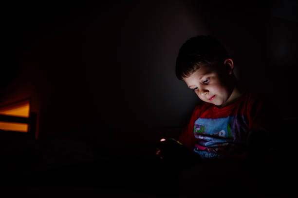 istock Addicted little boy playing games on phone in bed at night. 1411834257