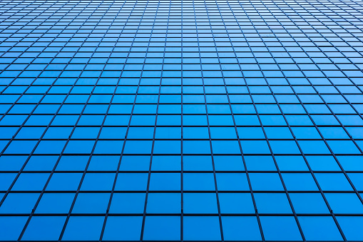 Perspective of the facade of a modern skyscraper with large reflected surfaces made up of regular rectangles.