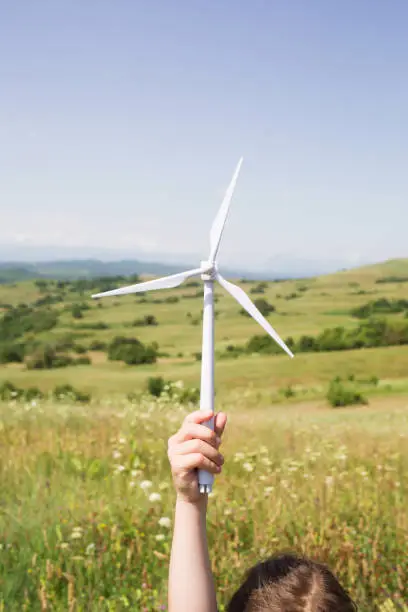 Photo of 3d model of wind turbine in hand of child against background of nature, fields and mountains. concept of environmentally friendly energy