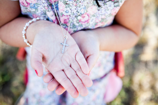 Young girl holding in her hands a silver necklace with a cross on it.