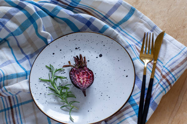 Glazed and roasted young red beet on a plate, baked beet on the towel on the wooden background. Roasted young half beetroot with rosemary and sea salt served on the table.