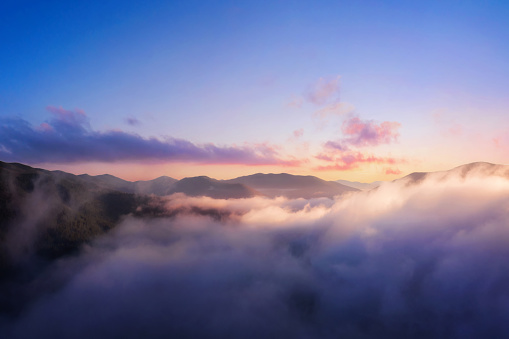 Mountains in low clouds. Mountain landscape with dramatic cloudy sky, peaks in fog and bright sunlight at dawn in the morning. Aerial view. Travel and tourism.