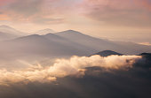 istock Mountains in low dense fog at morning sunrise. Beautiful landscape with mountain peaks in fog. 1411846592