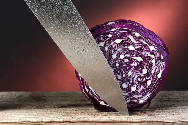 Closeup of a head of red cabbage and a carving knife. Horizontal format on a rustic wood surface and a warm light to dark background. The cabbage and knife are covered with mist.