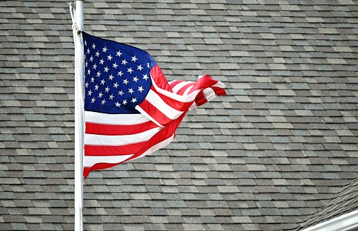 American flag in front of gray roof shingles.