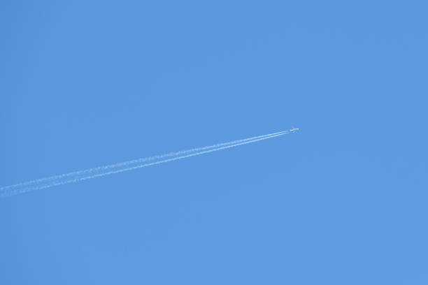 istock Distant passenger jet plane flying on high altitude on clear blue sky leaving white smoke trace of contrail behind. Air transportation concept 1411857207
