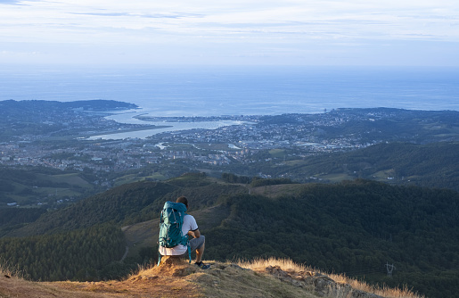 Sitting hiker at sunset contemplating the city and the sea