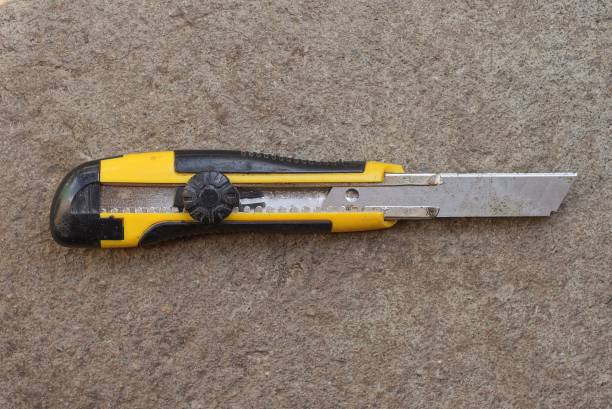 one yellow black stationery knife with a blade lies on a gray stone table