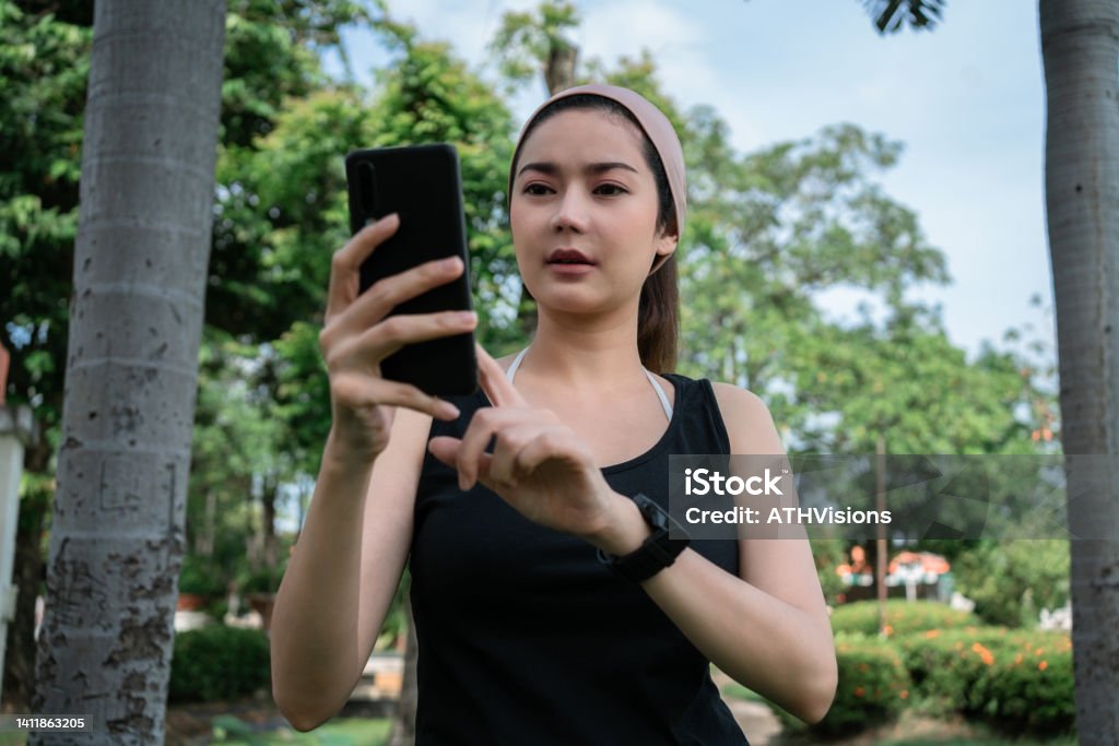 Adult woman watching stock market on mobile phone while  having morning run exercise Southeast Asian adult woman watching stock market on mobile phone while  having morning run exercise. free time passive in come Device Screen Stock Photo