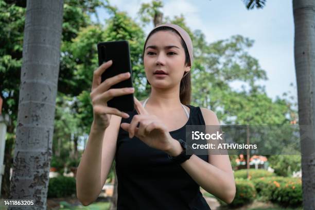 Adult Woman Watching Stock Market On Mobile Phone While Having Morning Run Exercise Stock Photo - Download Image Now
