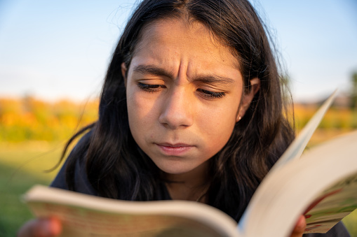 Pre Teen Girl Squints to Read Words in a  Book. Squinting because of poor eyesight can be caused by Myopia.