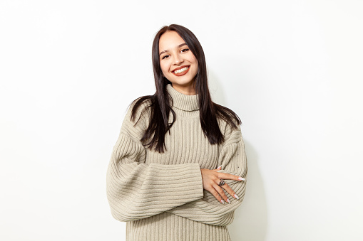 Young woman with long black hair in a beige sweater studio portrait on a white background