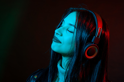 Young woman with long black hair listening to music with headphones close-up studio portrait on black background