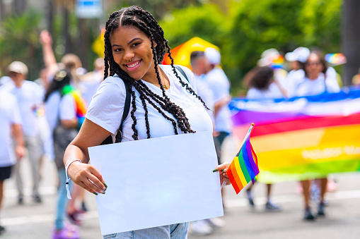 Smiling young afro-latinx woman holding a white cardboard in a pride parade