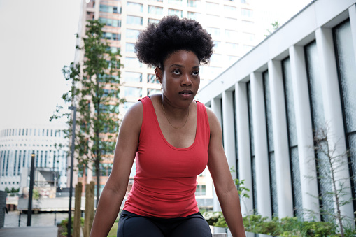 Portrait of young black woman doing exercise in an urban environment. Overcoming concept. Curly hair and red sleeveless t-shirt.