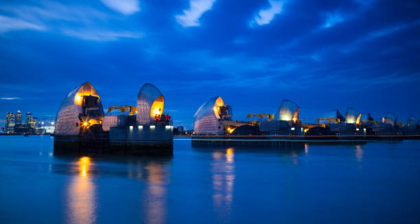 Section of the River Thames Flood Barrier at dusk with Canary Wharf and O2 Arena in the background, London, England, United Kingdom, Europe Section of the River Thames Flood Barrier at dusk with Canary Wharf and O2 Arena in the background, London, England, United Kingdom, Europe greenwich london stock pictures, royalty-free photos & images