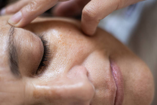 close up of a mature woman of arab ethnicity receiving a facial massage during a beauty and relaxation treatment in a spa. she has sun spots and age spots on her skin - ogen dicht closeup vrouw 50 jaar stockfoto's en -beelden