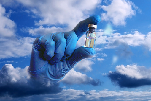 A hand in a blue medical glove sticks out of the clouds and holds out a vial of vaccine. Collage.