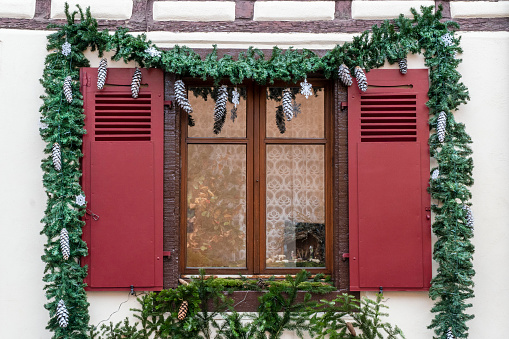 window with red blinders decorated with pine fir and cones for new year, exterior of a house