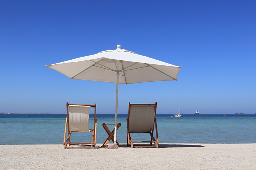 Beach chairs with an umbrella and a small table. Boats in the background.