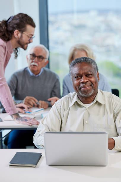 istock A senior african student smiling at the camera while group of multicultural senior students is discussing a programming project with an educator in the classroom. 1411880984