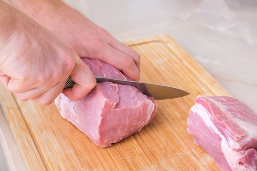 A man cuts meat with a knife on a wooden board. Preparation of minced beef and pork for cutlets, meatballs, chops.