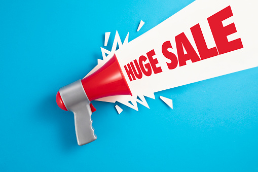 Red megaphone with colored papers and huge sale text on blue background