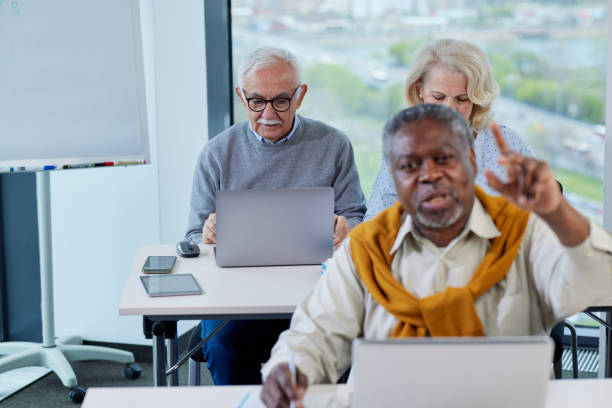 istock Seniors sit in a classroom and talking about project on the laptop while a multicultural senior student in foreground asking questions. 1411881134