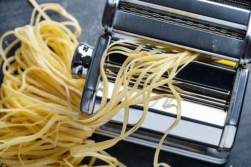 Homemade pasta in pasta machine on dark background.