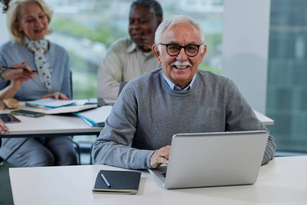 istock A senior man is working on a laptop while having a retraining class with a multicultural group of senior people in the classroom. 1411882088