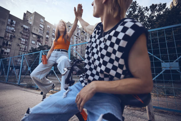 Teenage friends are sitting in the urban exterior and giving high five to each other. stock photo