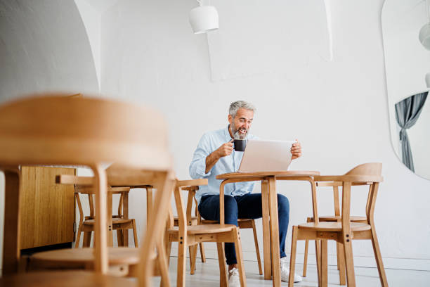 istock Attractive mature man sitting in coffee shop and using laptop computer 1411884100