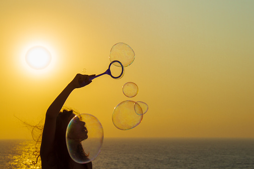Caucasian girl blowing soap bubbles by the sea at sunset in Pomos, Cyprus