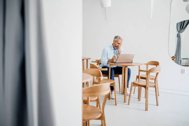 istock Contemplating businessman in the restaurant feeling sad. Full concentration on work. Confident mature man working on laptop while sitting at his working place in office. Tired manager sitting in restaurant surrounded with coffee and laptop computer having 1411884370
