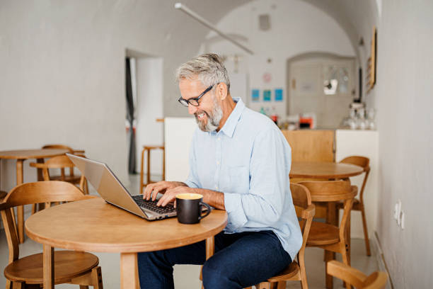 istock Attractive mature man sitting in coffee shop and using laptop computer 1411884400